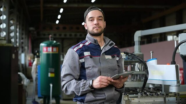Portrait of a young worker of an assembly line at a factory for the production of various products. Young white man with tablet controls production processes