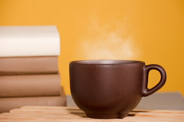 Brown cup of coffee or tea with hot steam, on the table, with books