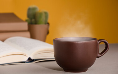 desk with cup of coffee or tea with hot steam , open books cactus, orange yellow background