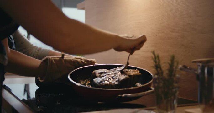 Female cook saucing beef steak kitchen pan stove close up slow motion