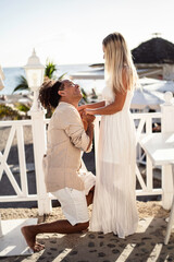 Romantic scene of a happy man making proposal to his beautiful woman on the beach.  Multiethnic couple.