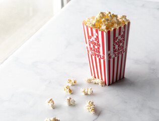A tall carton of freshly popped popcorn against a sunny window.