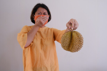 woman covering her nose from smelly Durian fruit in her hand - obrazy, fototapety, plakaty