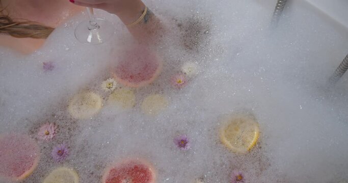 A woman in a bubble bath drinking a glass of white wine, down shot