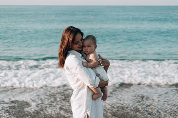 A young mother walks along the beach with a small child in diapers. Mother day. Family with one child. Happy childhood with mommy. Walking ocean wave