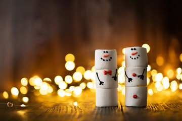 Marshmallow best friends. Two funny marshmallow snowmen. New year greeting card. Christmas winter holiday decoration. Christmas lights.