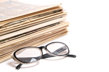 Stack of old newspapers and reading glasses on a white background.