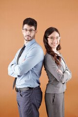 Portrait of confident young business colleagues standing back to back, crossing arms and smiling at camera