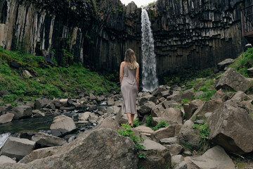 beautiful girl in a dress next to Svartifoss waterfall in the Skaftafell National Park, iceland