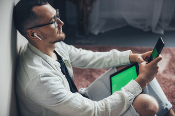 Side view of an businessman sitting on floor leaning from wallat home using digital tablet and phone while planning project. Online education. Home concept