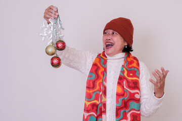 Woman in warm clothes and Santa's hat happily playing some Christmas ornaments