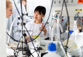 Intelligent yuong Chinese girl working with reagents in test tubes during chemical experiment with...