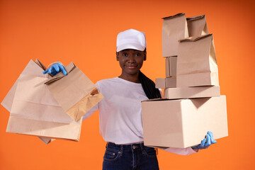 delivery, service, shipping and people concept - Smiling African-American courier woman in a white cap and blue gloves holding a large number of boxes and packages on orange background with copy space