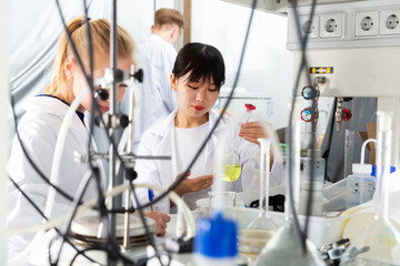 portrait of intelligent young Chinese girl working with reagents in test tubes during chemical...