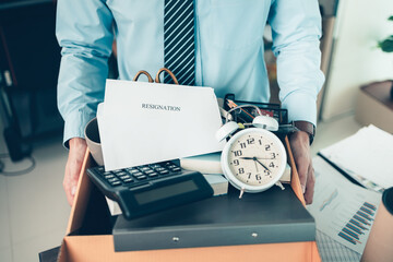 Unemployed hold cardboard box and resignation letter, dossier, alam clock, coffee cup, calculator and drawing tube in box. Quiting a job, businessman fired or leave a job concpet.
