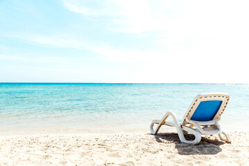 A lone white blue sun lounger stands on the seashore right next to the water. The concept of a beach holiday by the sea or ocean. Private beach of the hotel. Quiet calm sea side. High quality photo