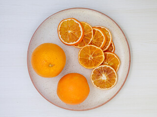 Dried thin slices, heap of orange fruit chips on white plate and two whole fruits on light background. Healthy food and snacks. Flat lay top view, close up, Minimalism
