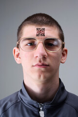 Young man with glasses presents a tattoo with a QR code on his forehead.