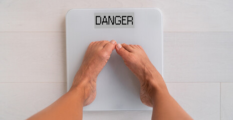 Unhealthy weight woman weighting herself on bathroom scale. Top view of feet anxiety due to obesity...