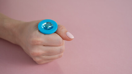 A woman is holding a blue butt plug with a crystal on a pink background. Adult toy for alternative sex