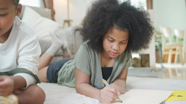 4K Happy African family cute child girl kid sibling lying on the floor using color pencil drawing and painting together on the paper. Little sister enjoy and fun with leisure activity together at home