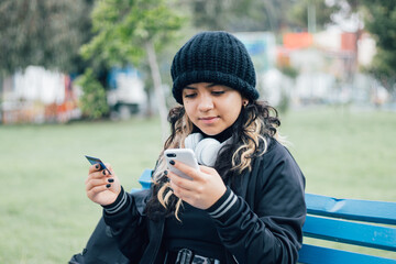 Latin teenager college girl sitting on a bench at the park buying online with credit card