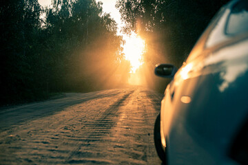 dusty dirt road on a beautiful sunset behind the forest, in the front and background silhouettes of cars