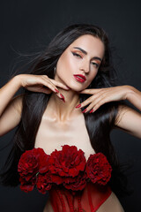 Naklejka premium Beautiful brunette woman with a bouquet of red rose flowers in red corset. Long hair, nude slim body art portrait