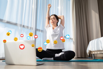 Young woman in sportswear doing yoga live online. Indoor. Emoticons and emojis fly around the laptop. Bottom view. The concept of social networks, online training and blogging