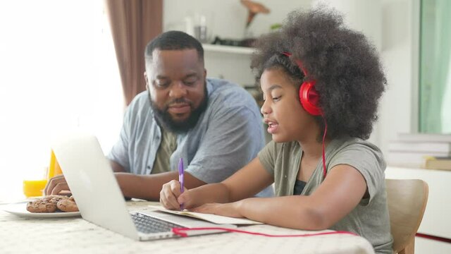 4K African family spending time together at home. Father helping little daughter online study on laptop computer in living room. Cute child girl kid studying homeschooling with using online E-learning