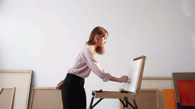 Painting lesson. Female artist. Professional art school. Concentrated woman creating on canvas with slate pencil in light room interior.