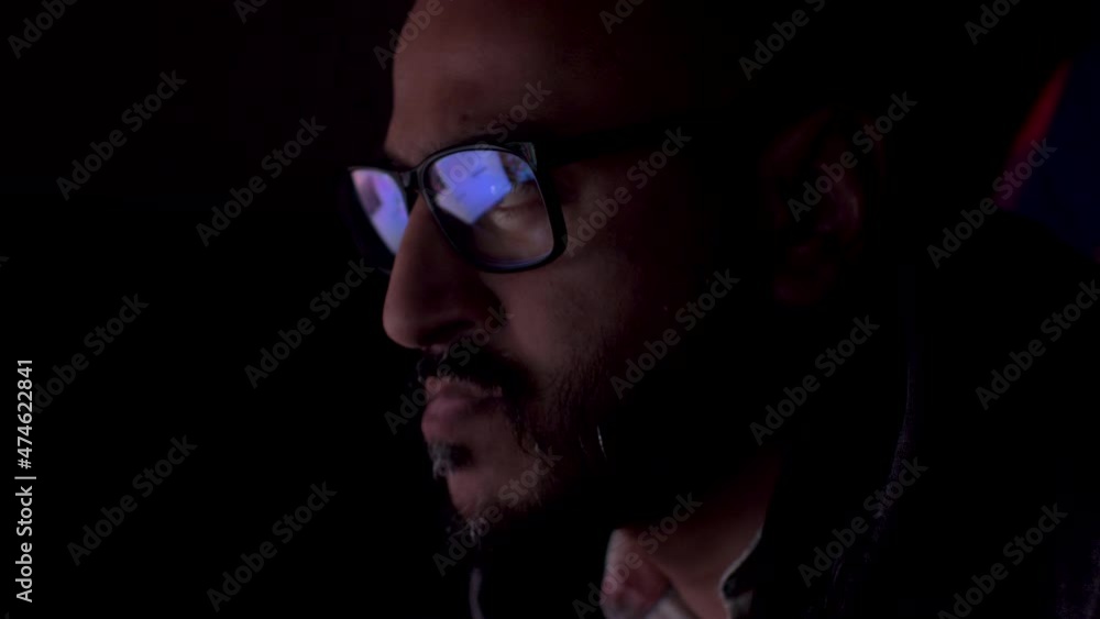Poster serious man with reflection of laptop screen with website data in glasses working late, close up. in