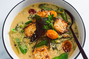 vegan thai green curry with pan fried silken tofu and freshly picked vegetables, healthy plant-based food