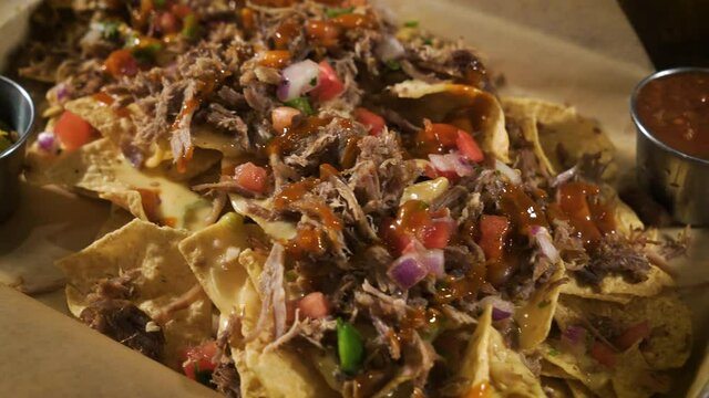 Nacho pile of corn tortilla chips slathered with queso cheese sauce pulled pork and pico de gallo salsa, close up slider 4K