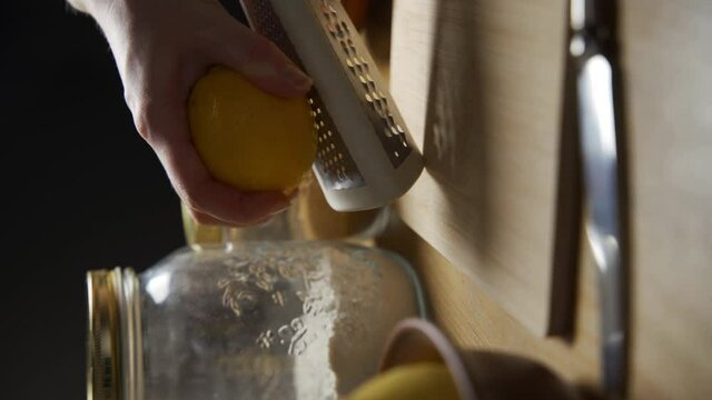 Video clip female hands grating lemon with stainless steel zester or grater over wooden cutting board. Healthy eating, Food ingredient preparing theme. Vertical shot