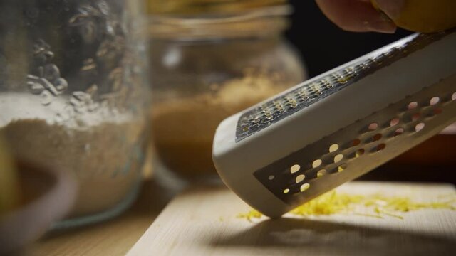 Video clip female hands grating lemon with stainless steel zester or grater over wooden cutting board. Healthy eating, Food ingredient preparing theme.