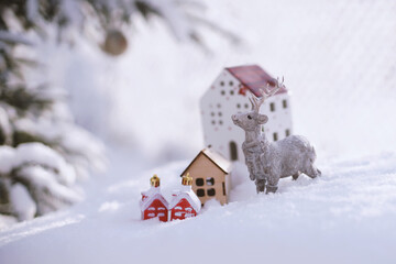 A deer figurine and toy houses stand on a table in the snow.