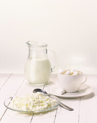 Fresh cow's milk in a jug on a white background with healthy cottage cheese and a cup of coffee with marshmallows