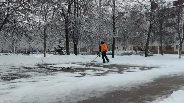 Utility worker in orange vest using shovel removes wet snow from public stop. Manual cleaning. Slush. Plus temperature in winter