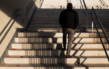 Rear view of adult man walking upstairs with sunlight and shadow
