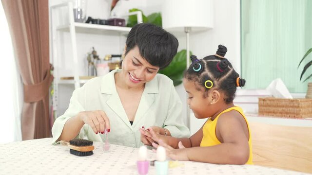 4K Happy family African mother applying nail polish to little daughter in living room. Mom and child girl kid enjoy and having fun leisure activity spending time together with beauty treatment at home