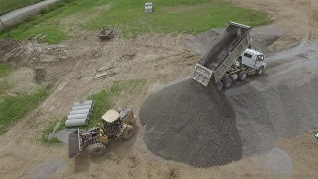 Aerial of dump truck unloading gravel off a inclined gravel ramp.