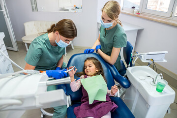 two young beautiful dentists girl in masks and gloves clean the baby's mouth.