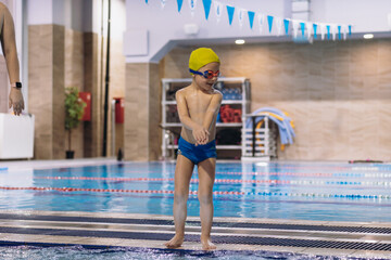 little caucasian boy wearing goggles going to dive into swimming pool