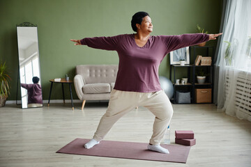 Full length portrait of active senior woman doing yoga at home and enjoying workout indoors, copy...