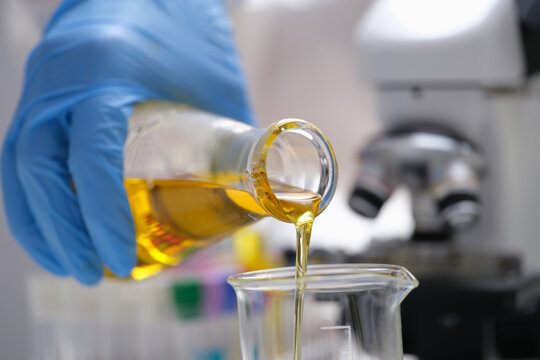 A hand in a glove pours a yellow liquid in the laboratory