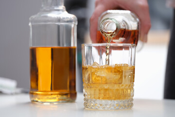 A hand pours a brown alcoholic drink into a glass