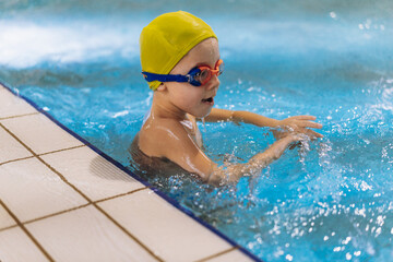 Fototapeta na wymiar little caucasian boy wearing goggles swimming in a pool