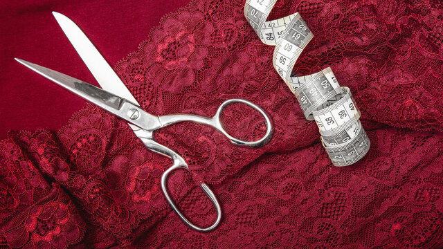 Creative sewing background, top view. Collection of various sewing tools , red, burgundy lace fabric, tape measure, scissors