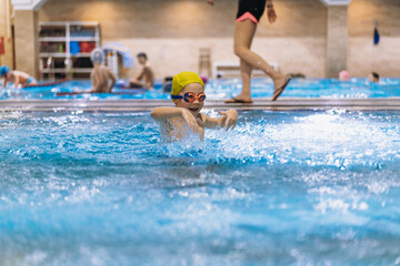 little caucasian boy wearing goggles splashing in small pool in sport centre